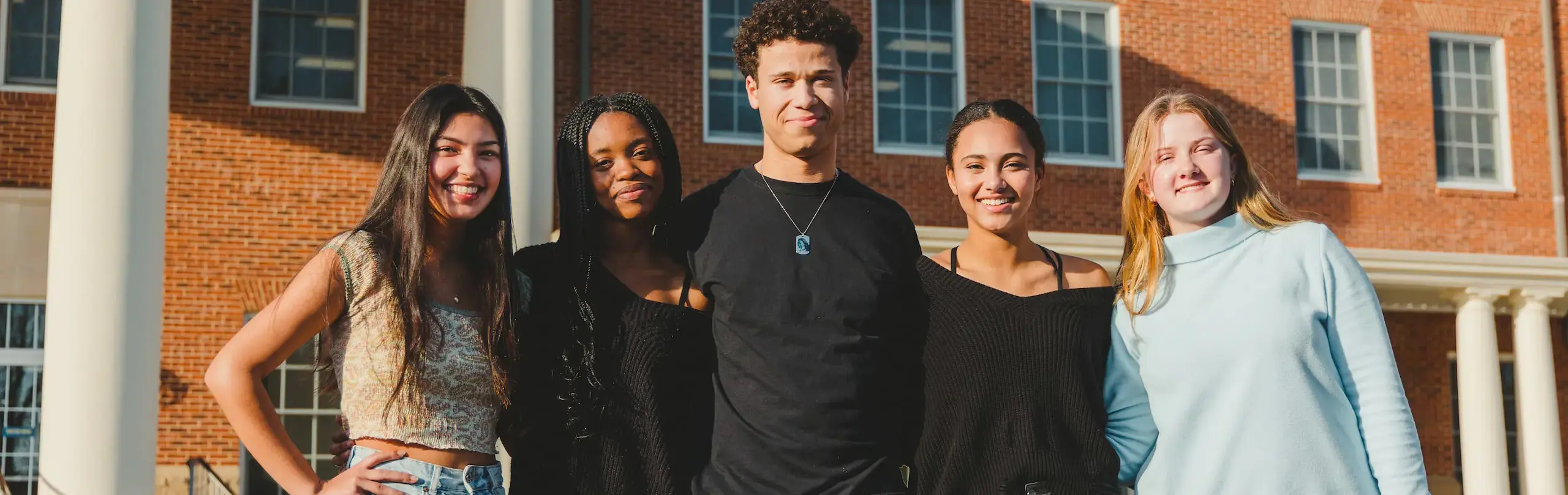 Group of diverse high school students smiling in front of Trinity School of Durham and Chapel Hill, showcasing the school's commitment to diversity and inclusion.