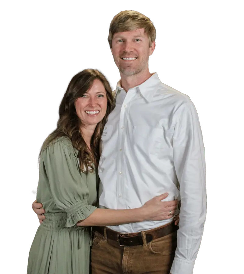 A smiling couple posing in front of a backdrop with the emblem of Trinity School, exuding a warm and welcoming atmosphere at a school event.