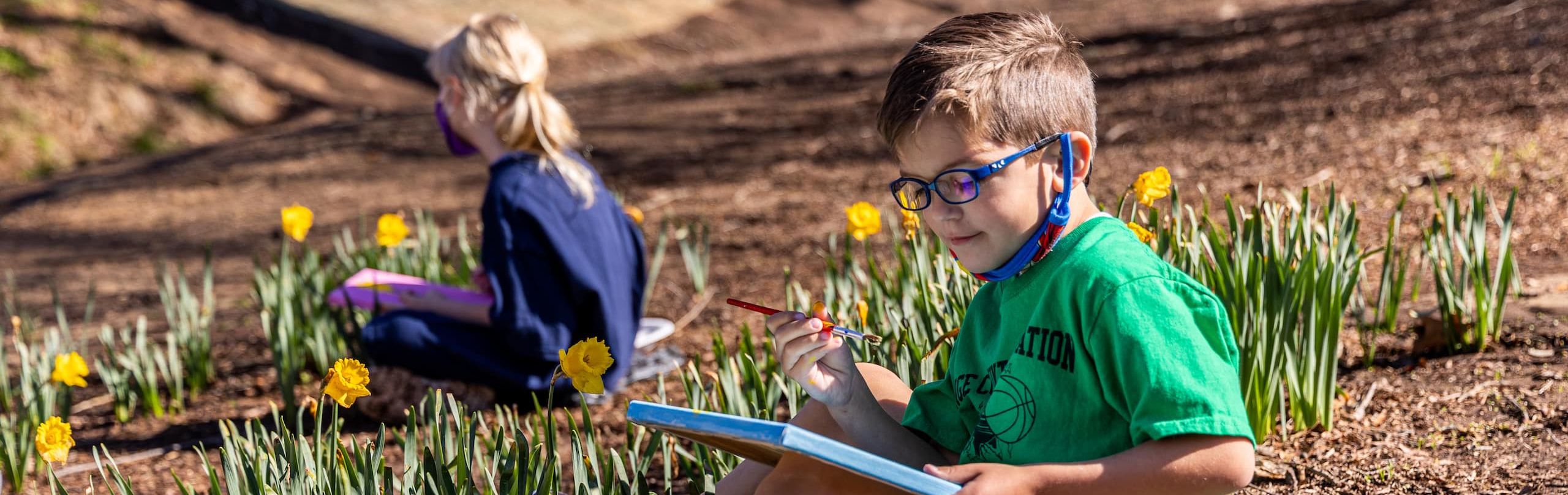 Trinity School Lower School student painting outside surrounded by daffodils