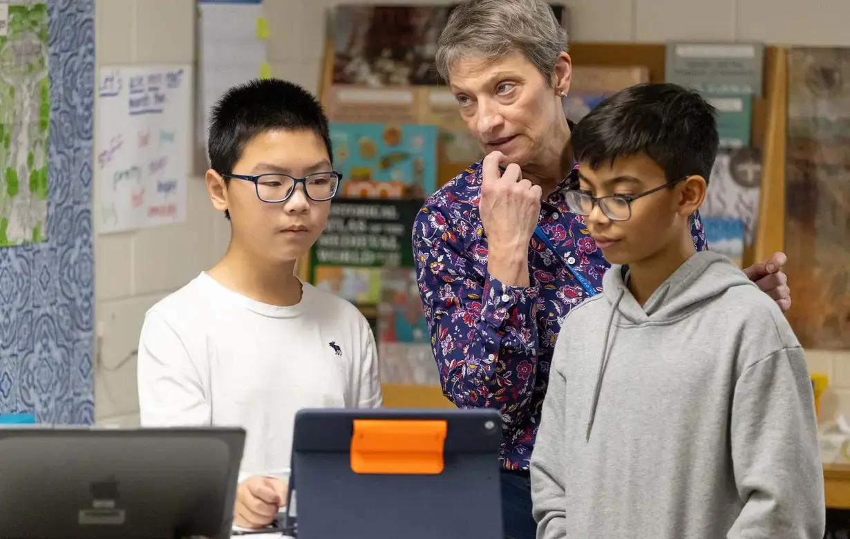 Teacher with two students in classroom looking at computer screens