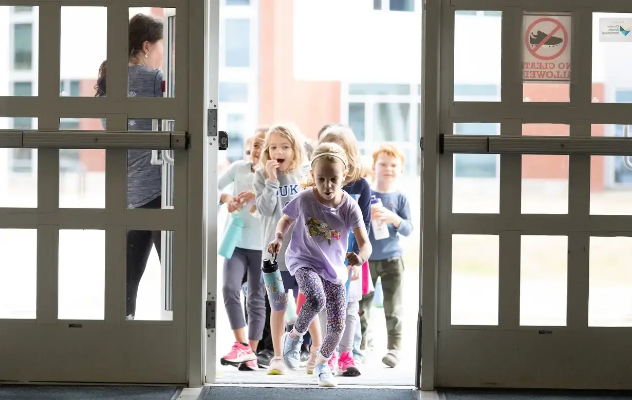 Group of Lower School Trinity students running through doors