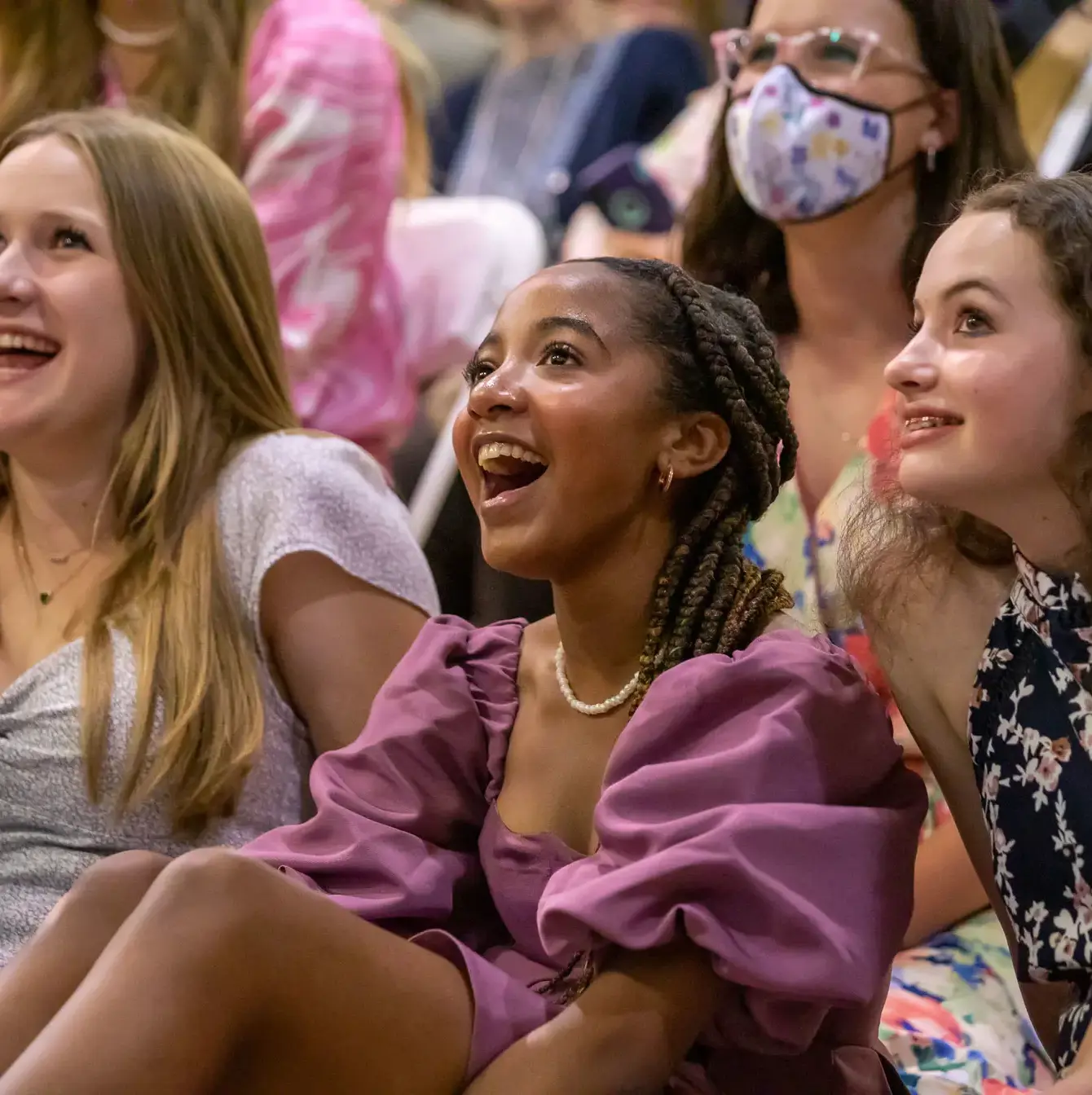 Three joyful teenage girls, dressed in colorful attire, are caught in a moment of laughter and delight while attending a school event, their expressions radiating happiness and excitement.