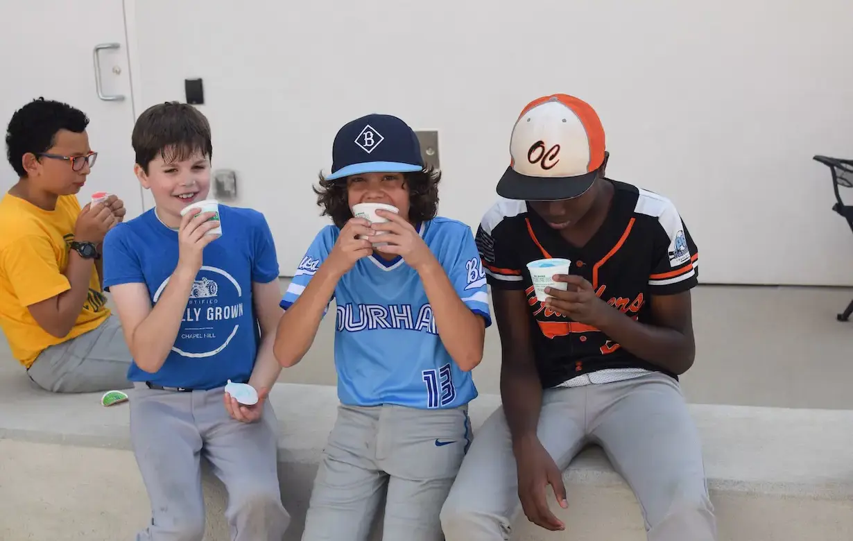 Three young boys are seated on a bench eating ice cream from tubs