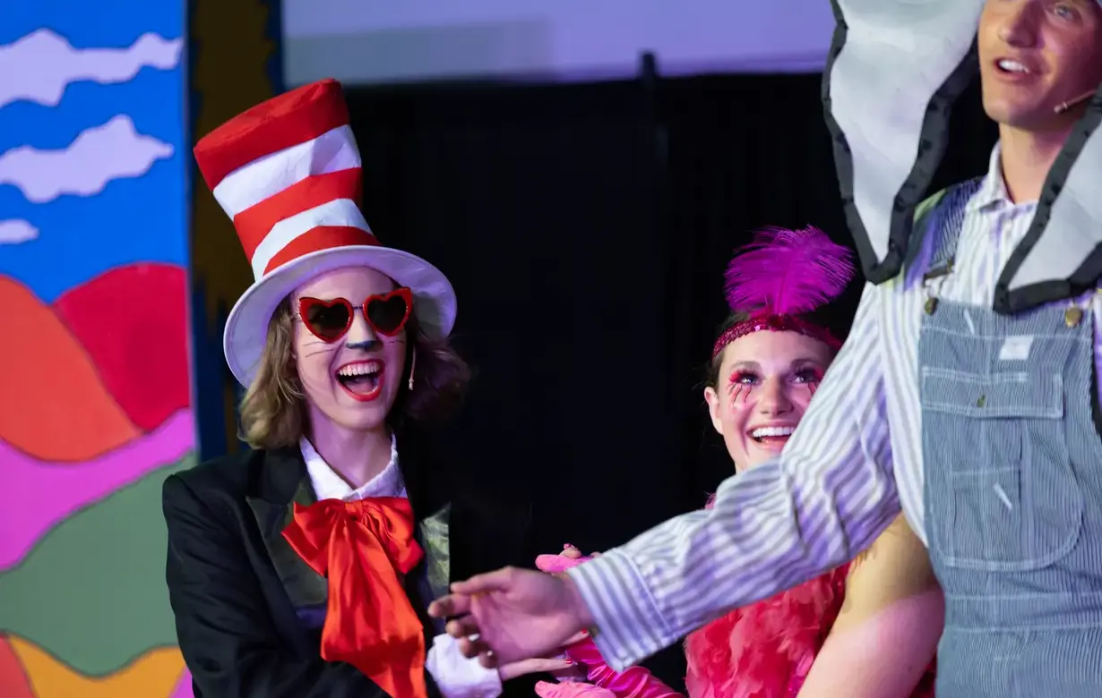 Performers in colorful costumes, including the Cat in the Hat and other Seussical characters, on stage during a musical theater performance.