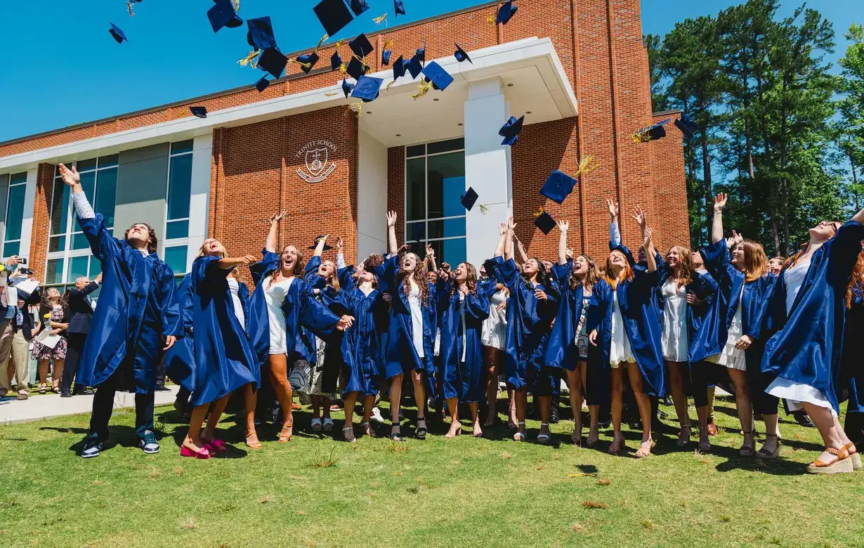 Exuberant high school graduates in blue gowns tossing their caps into the air, celebrating their commencement day with joy and a sense of achievement in front of the school building.